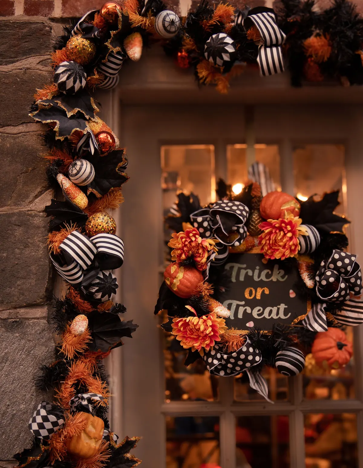 Glass-paned door framed by a black, orange and striped-ribbon garland, with a matching wreath and a small black plaque