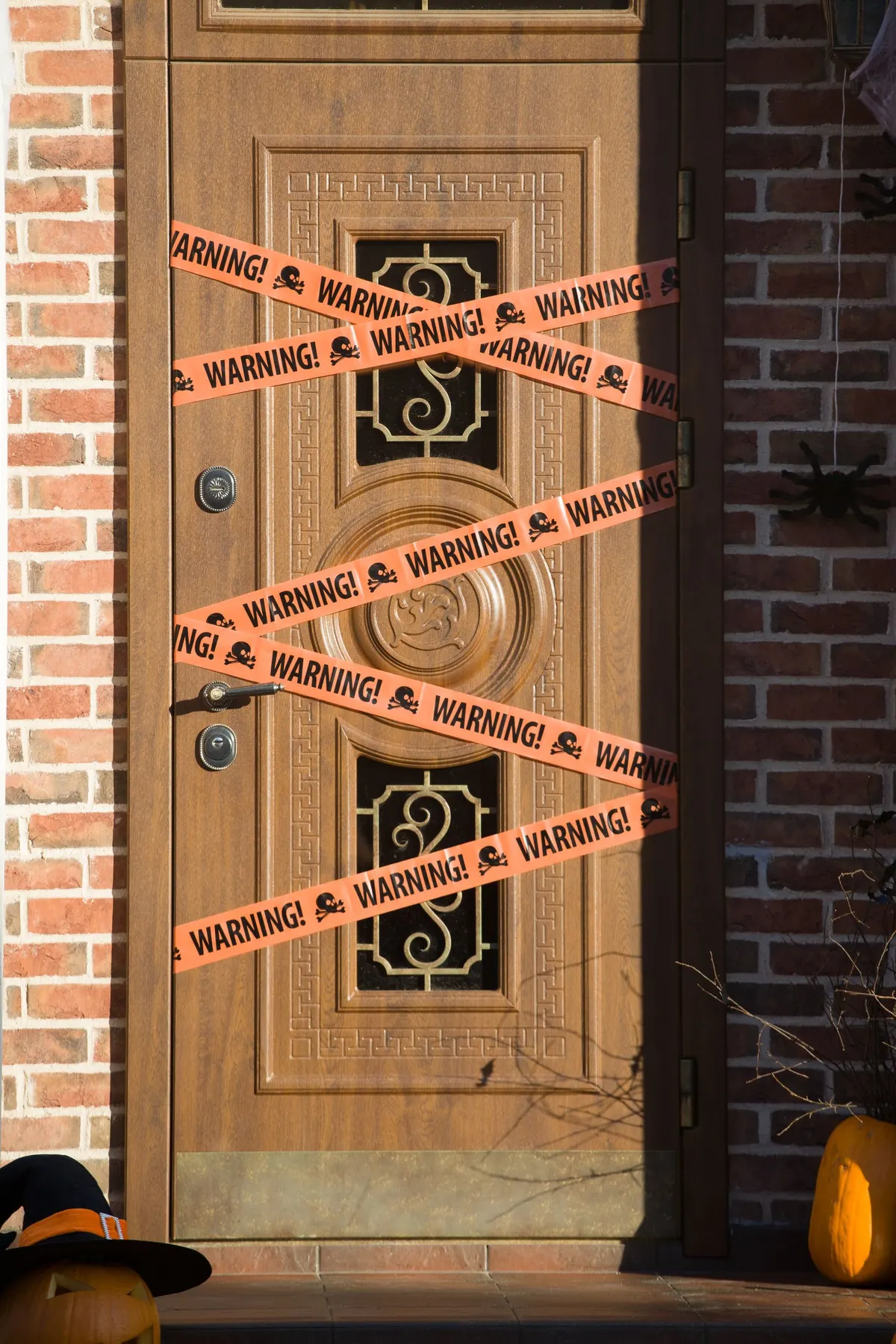 Carved wooden door crisscrossed with orange Halloween warning tape printed with skulls, between red brick walls