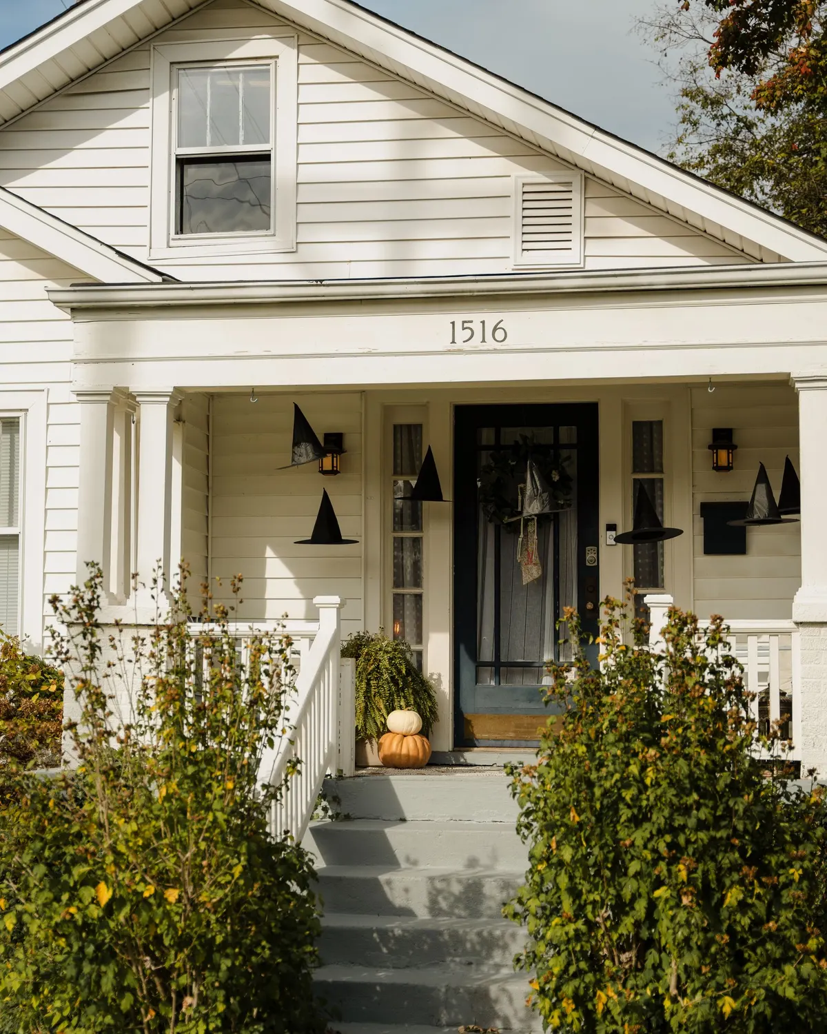 White porch with about seven black witch hats hanging at different heights around a dark glass door and wreath