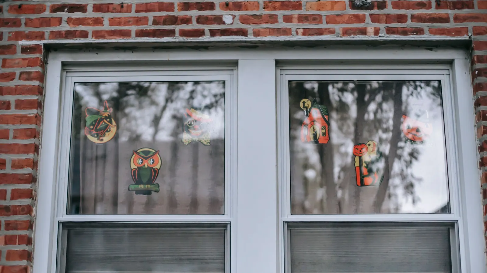 Two white sash windows in red brick with six vintage-style Halloween cutouts such as a witch, owl and cat