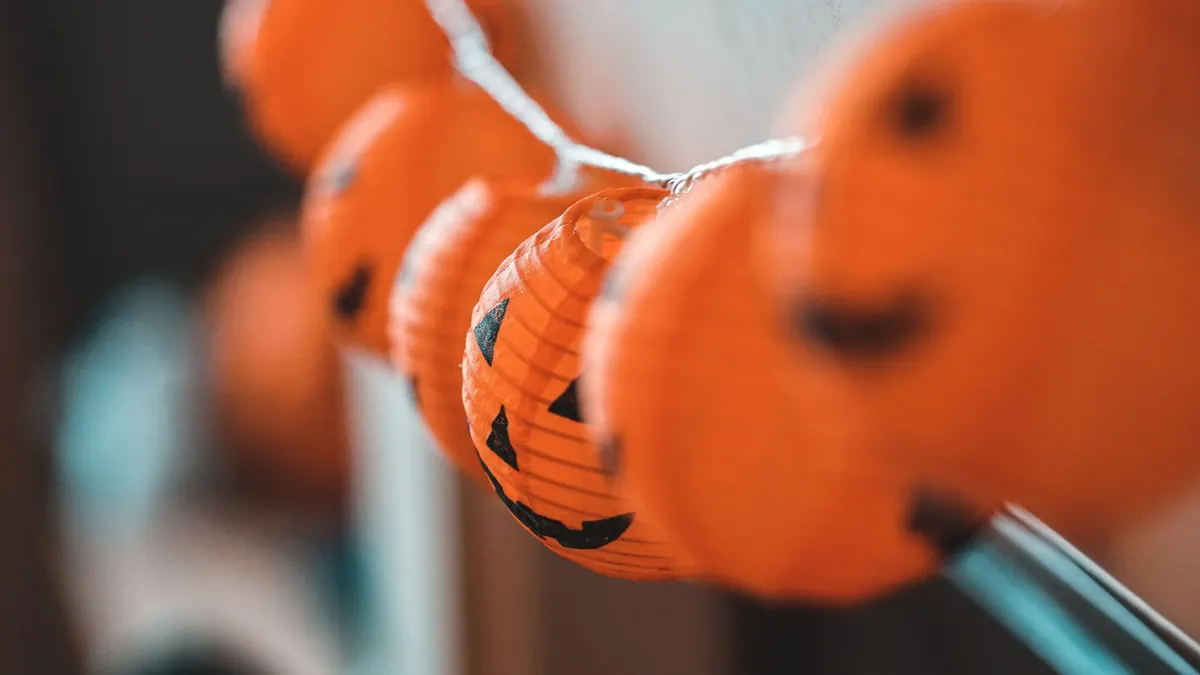 Seven orange ribbed paper pumpkin lanterns with black jack-o-lantern faces hanging along a white twisted wire