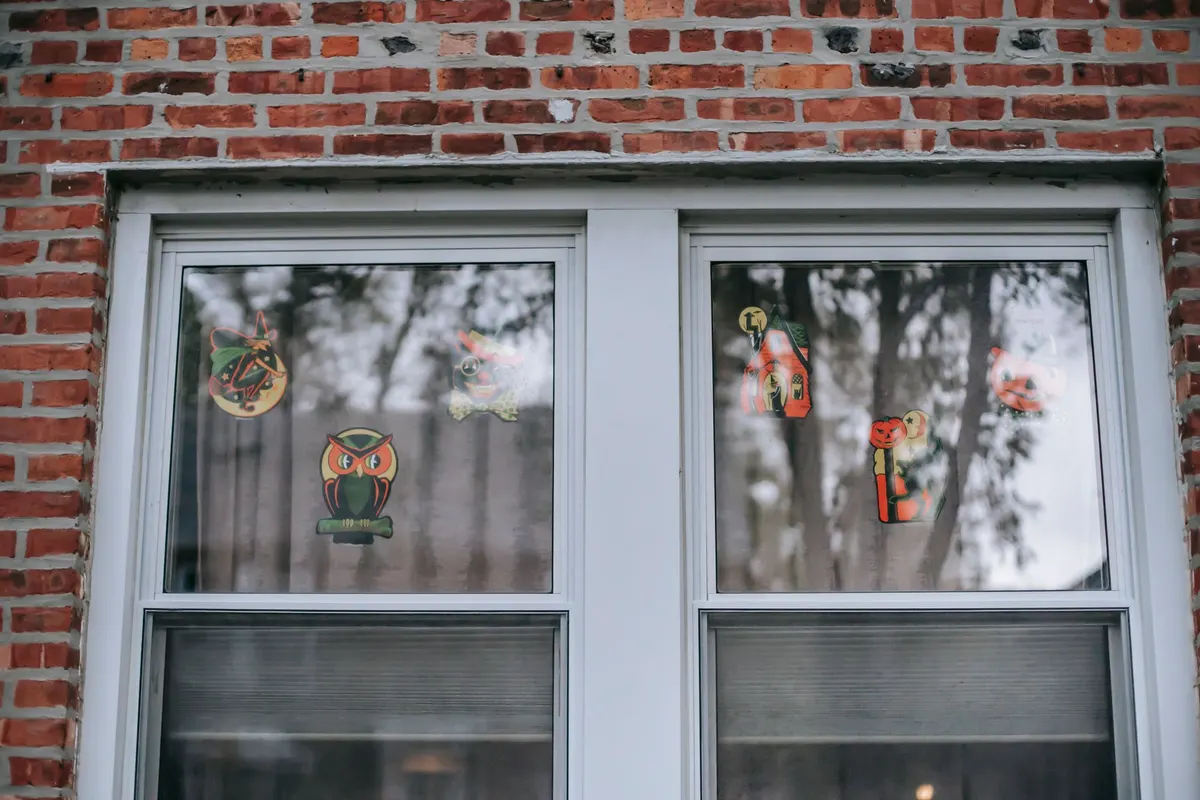 Two white sash windows in red brick with six vintage-style Halloween cutouts such as a witch, owl and cat