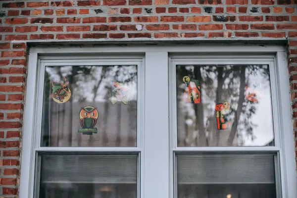 Two white sash windows in red brick with six vintage-style Halloween cutouts such as a witch, owl and cat