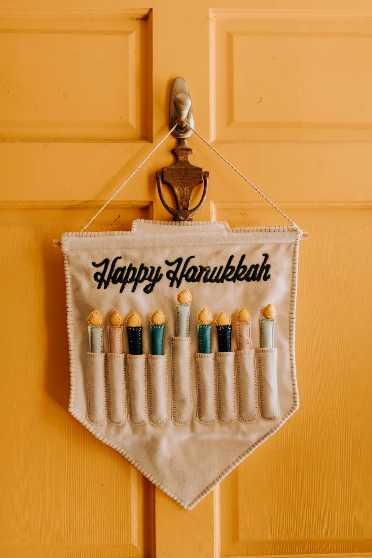 Cream felt menorah banner with nine felt candles and yellow flames hanging on a yellow front door
