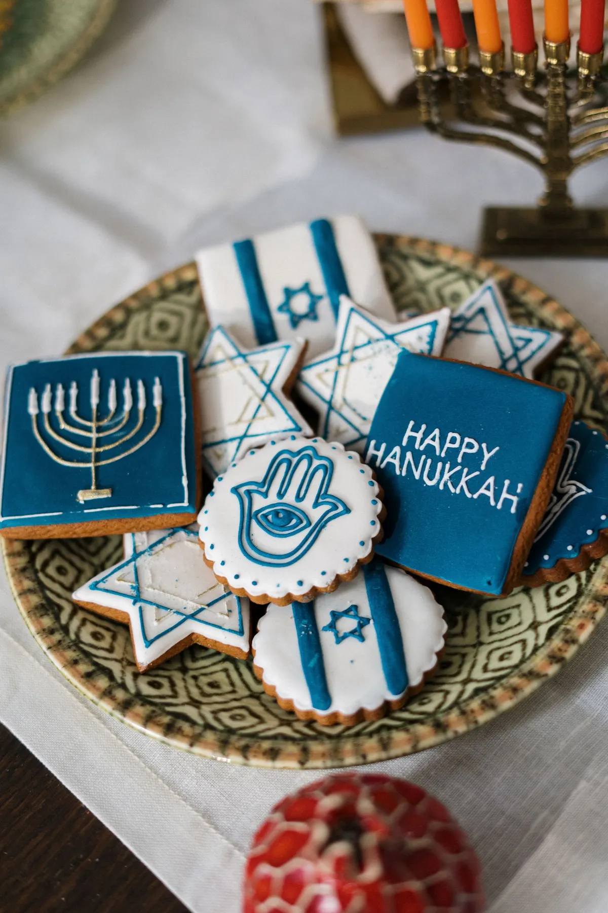 Blue and white iced cookies shaped like stars, a hand and a menorah on a green patterned plate