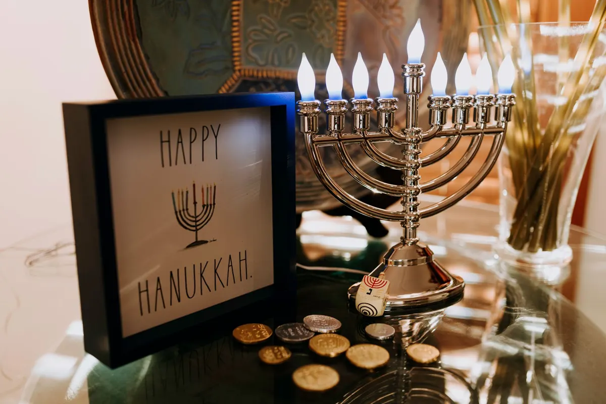 Silver electric menorah with nine flame-shaped bulbs beside a framed greeting, a dreidel and coins on glass