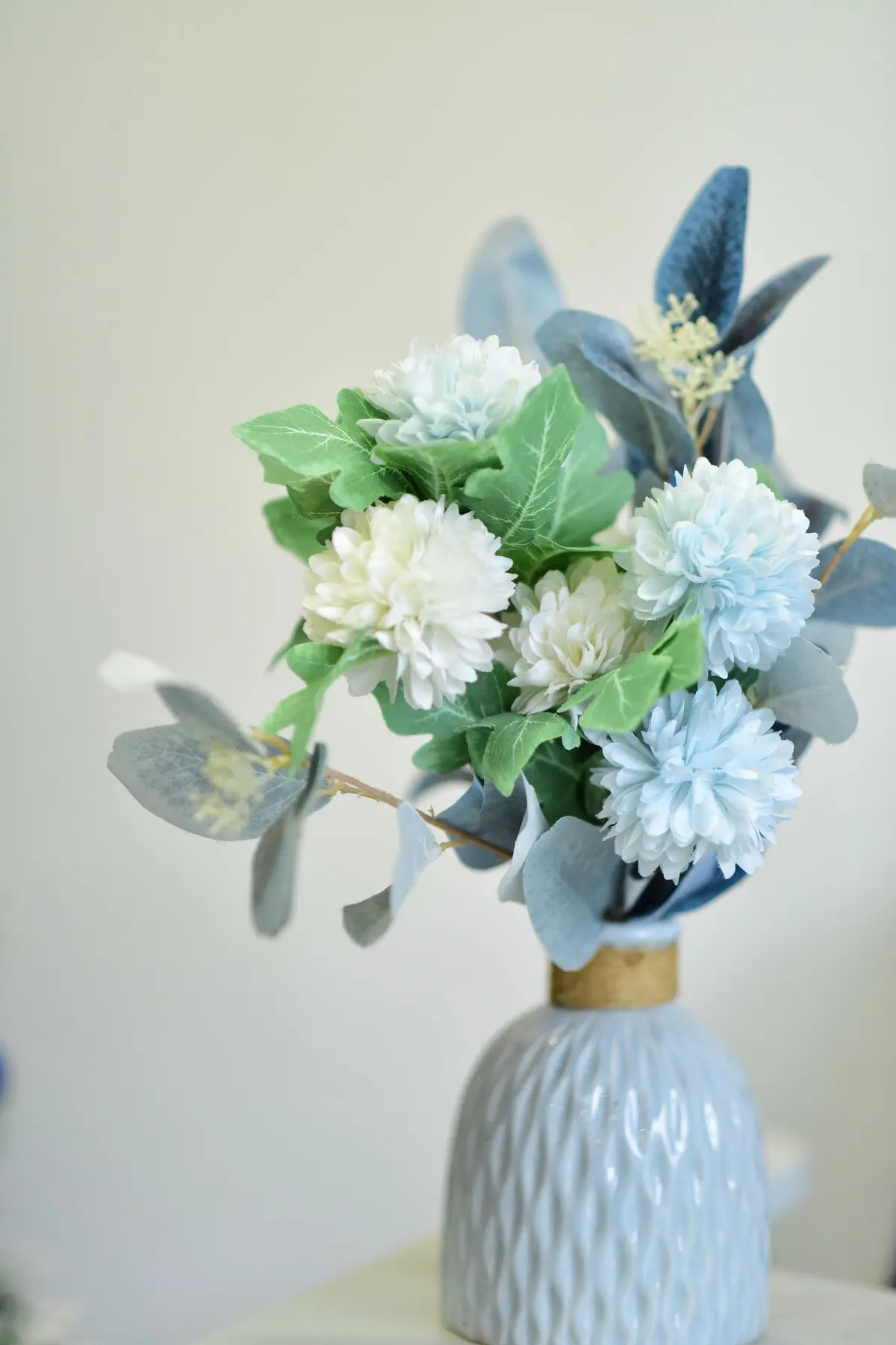 Pale blue textured vase with a gold band holding white and pale blue flowers and gray foliage