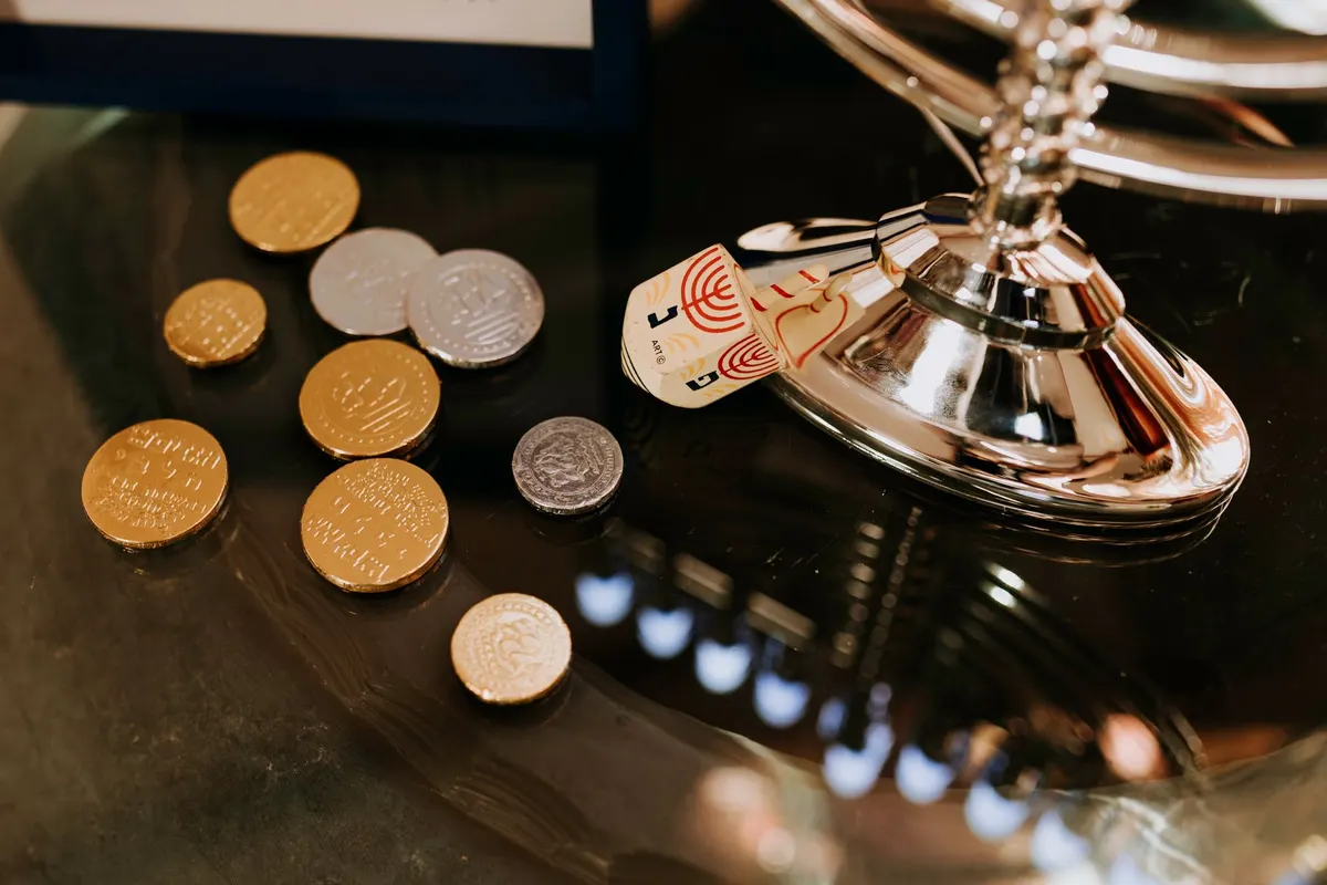 Six gold and three silver foil chocolate coins beside a cream dreidel on a glossy black surface