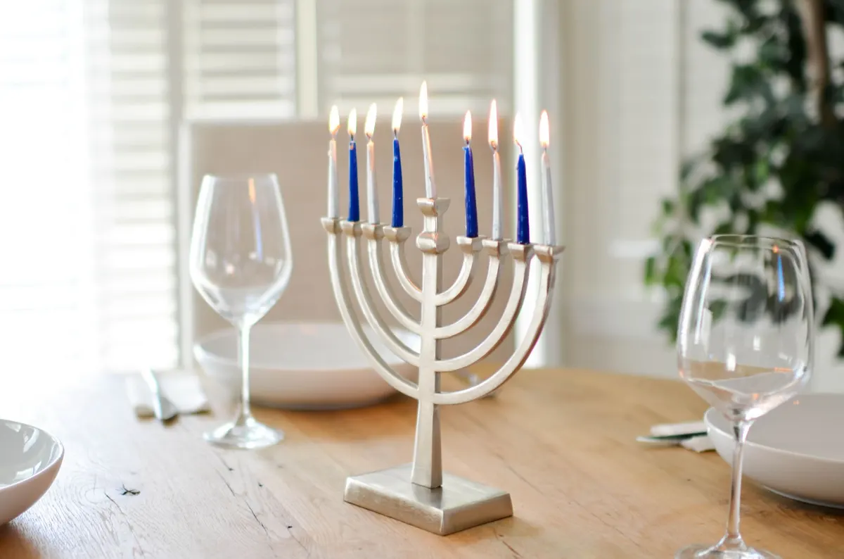 Silver menorah with four blue and five white lit candles on a dinner table with wine glasses