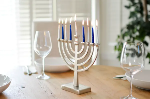Silver menorah with four blue and five white lit candles on a dinner table with wine glasses