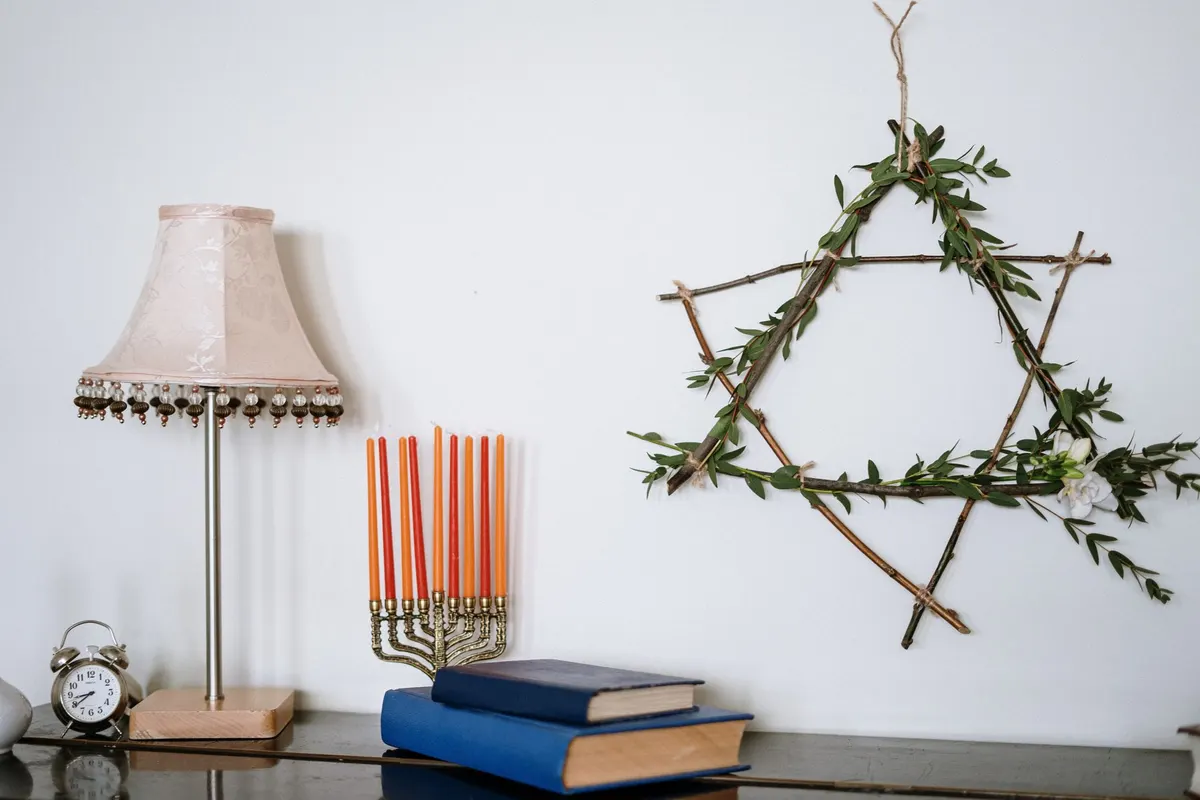 Brass menorah with orange and red candles on a dark cabinet with blue books, a lamp and a clock