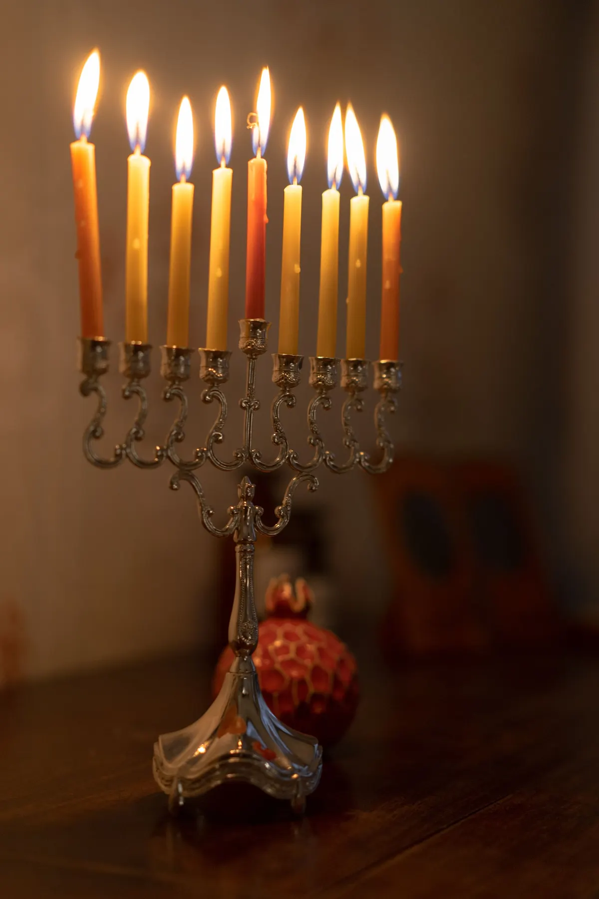 Ornate silver menorah with yellow, orange and red lit candles and a raised center candle on dark wood