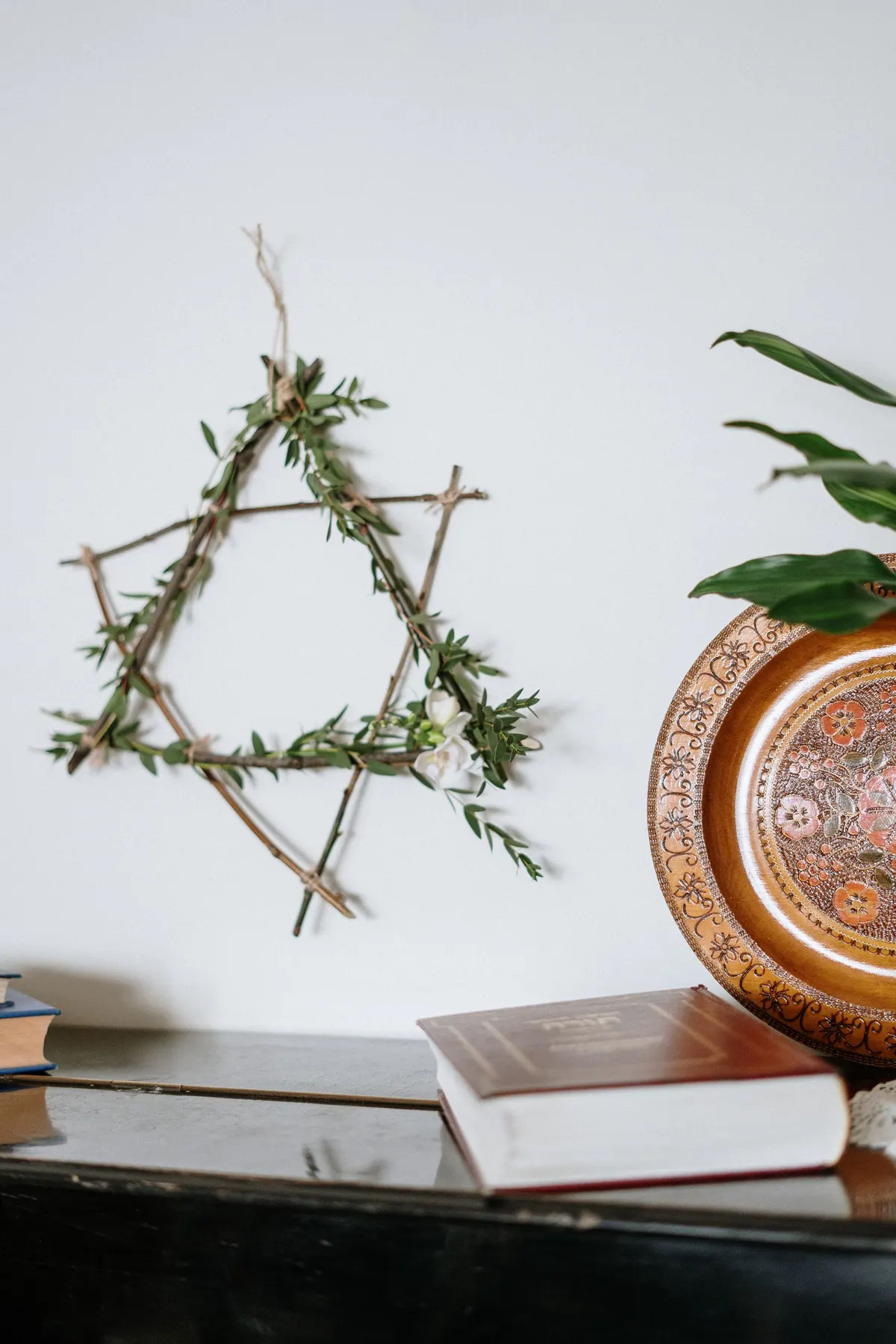 Six-pointed twig star with green leaves and white flowers hanging above books and a copper plate