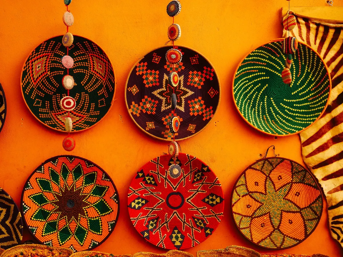 Six round woven plates in green, purple, red and orange patterns hung on an orange wall