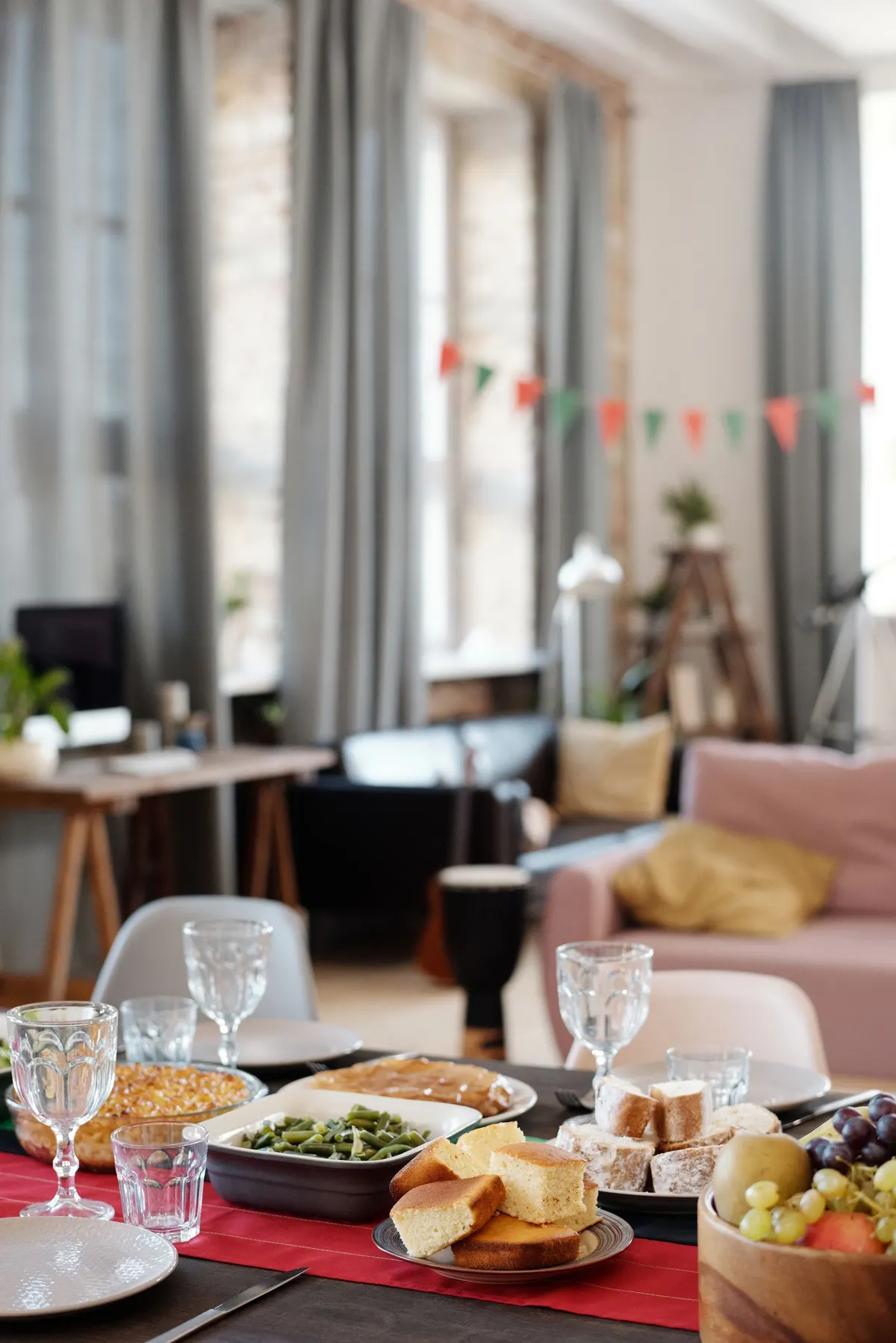 Dining table with a red runner and dishes below red and green pennant bunting across tall windows