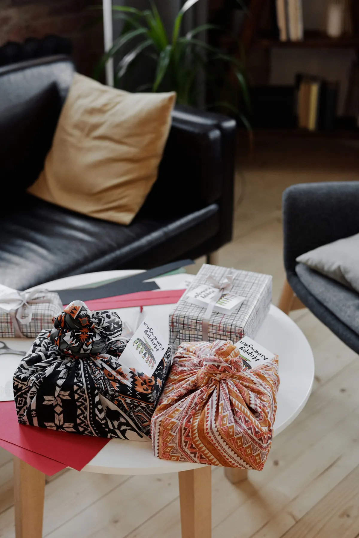 Fabric-knotted gifts and plaid boxes on a white table with red, black and green paper and scissors