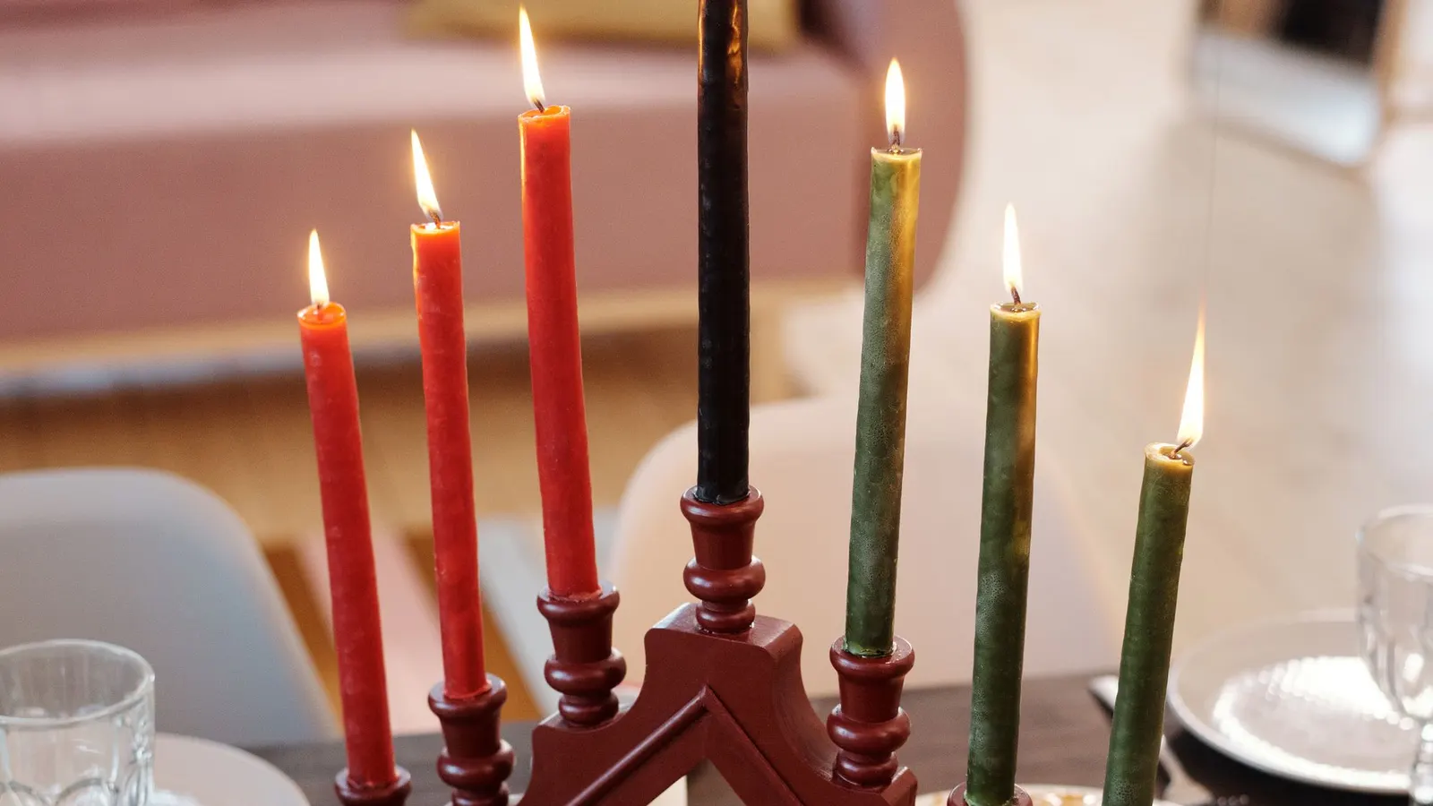 Lit wooden kinara with three red, one black and three green candles on a striped red, black and green runner