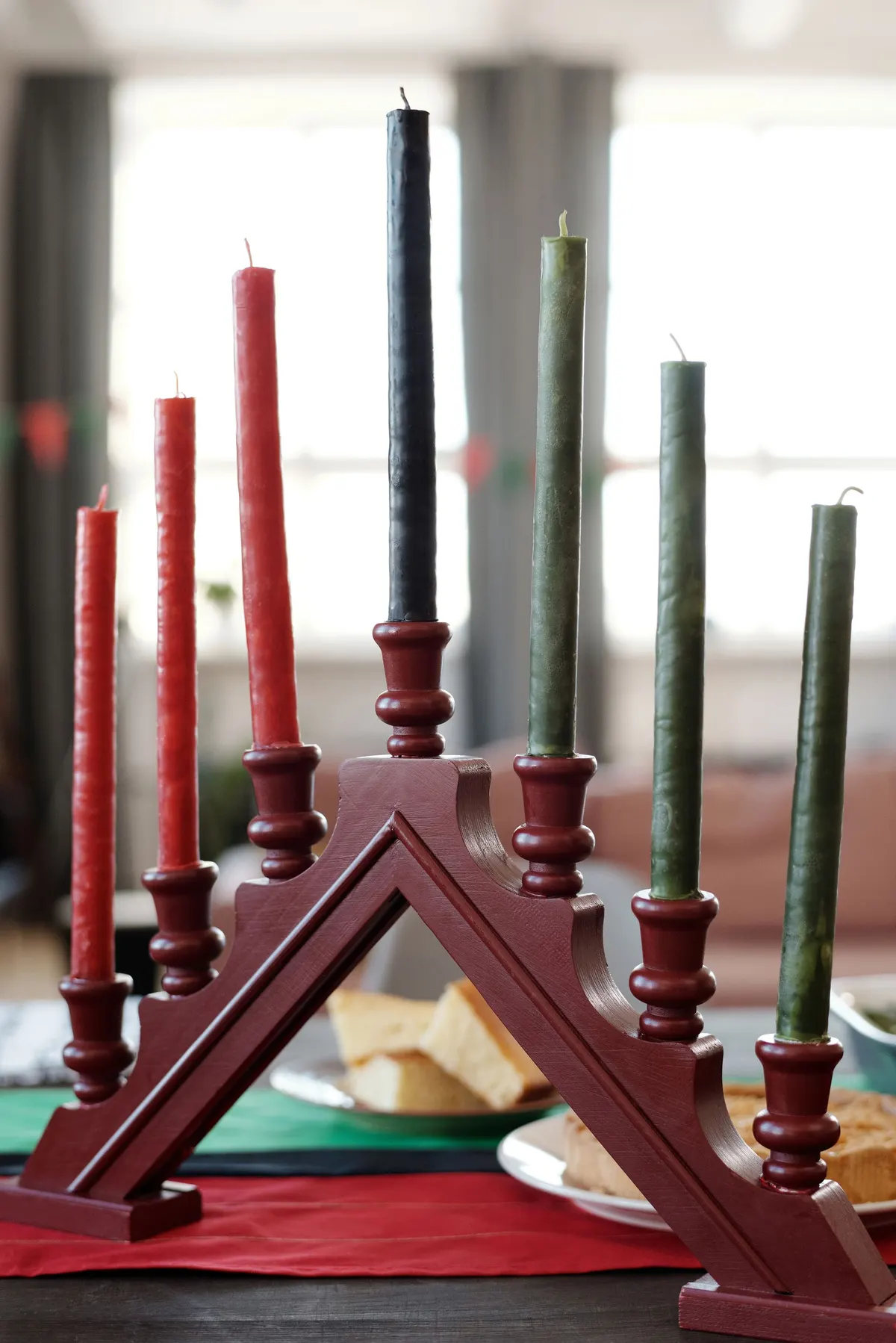 Peaked wooden kinara holding seven unlit red, black and green candles over green, black and red striped cloth
