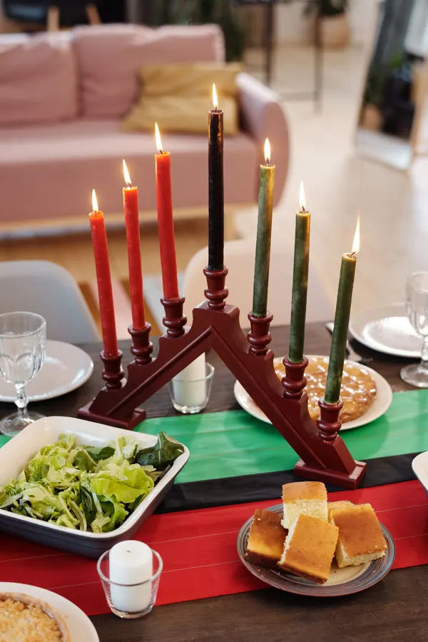 Lit wooden kinara with three red, one black and three green candles on a striped red, black and green runner