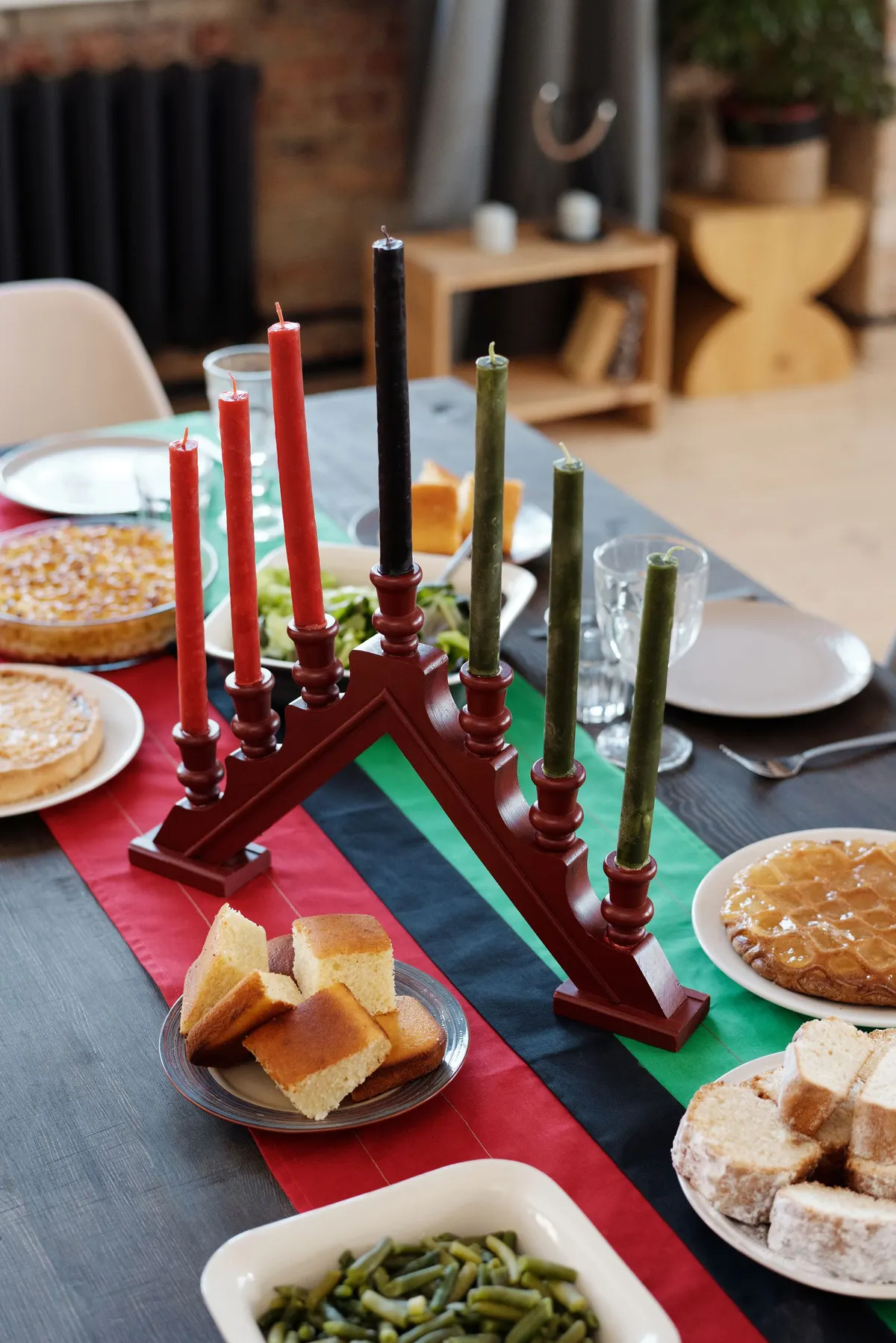 Unlit kinara on a red, black and green striped runner with cornbread, green beans and salad dishes