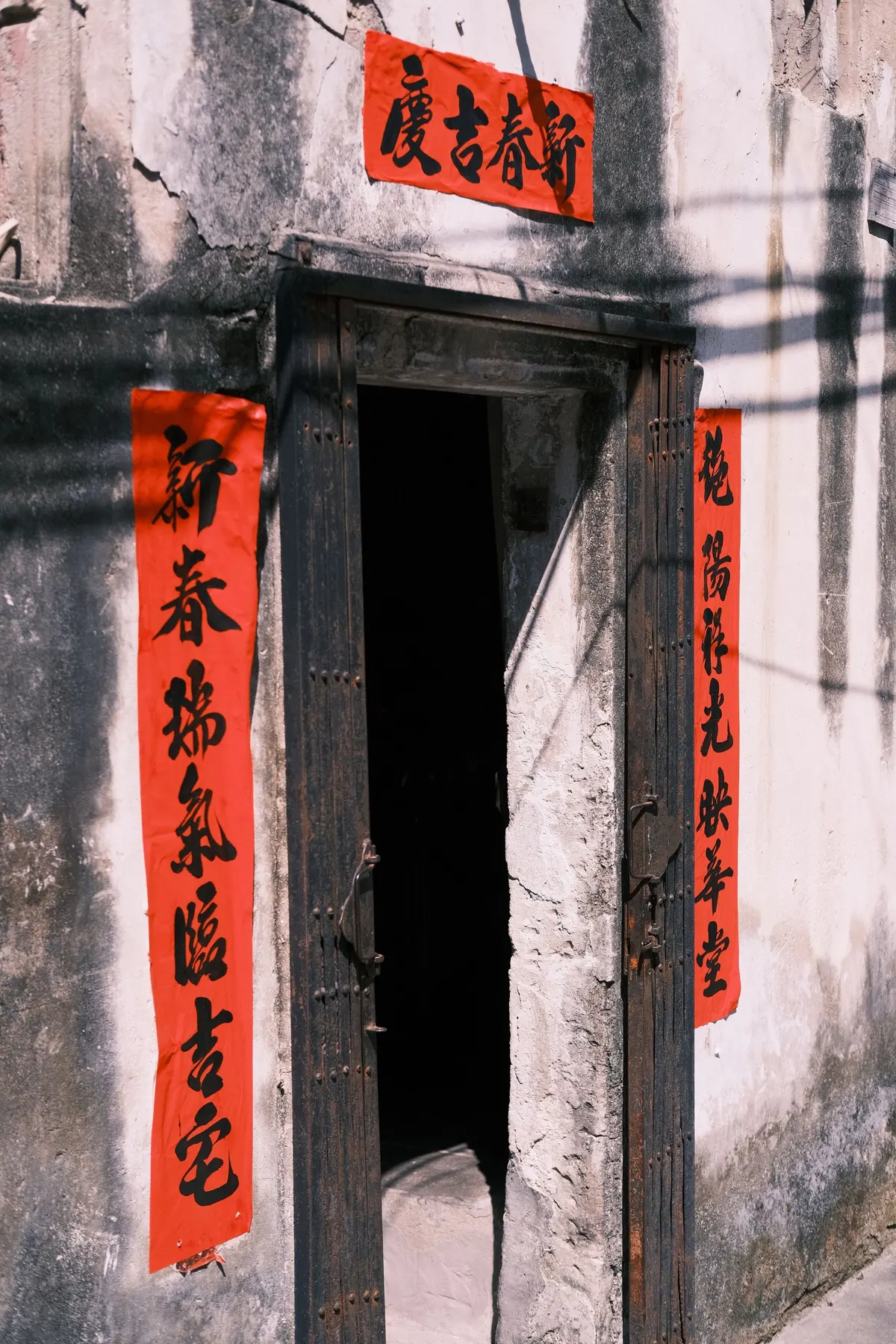 Dark doorway in a weathered white wall, framed by a red horizontal banner and two vertical couplet strips