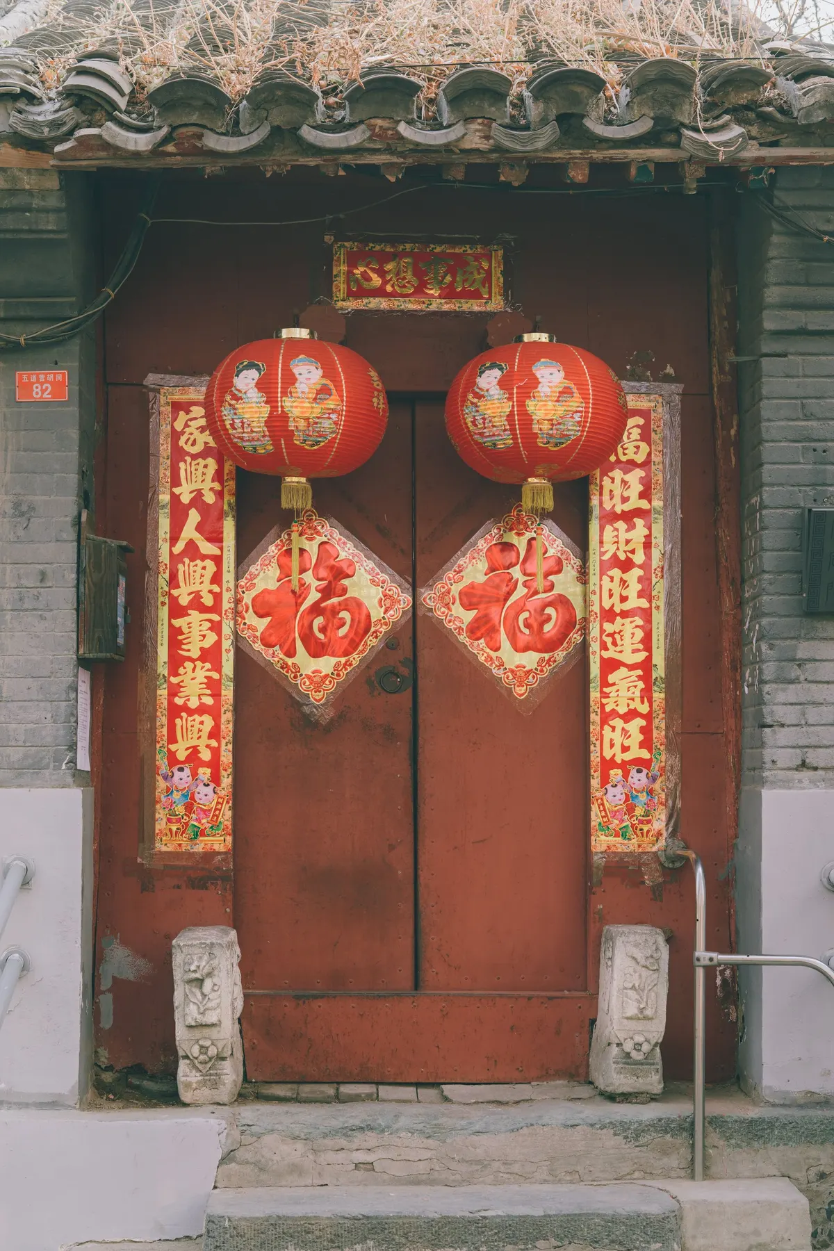 Weathered reddish-brown double door with two red lanterns, two diamond fu papers and red couplet banners