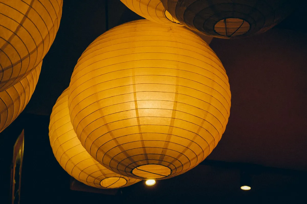 Six glowing yellow-orange round paper lanterns hanging close together under a dark ceiling