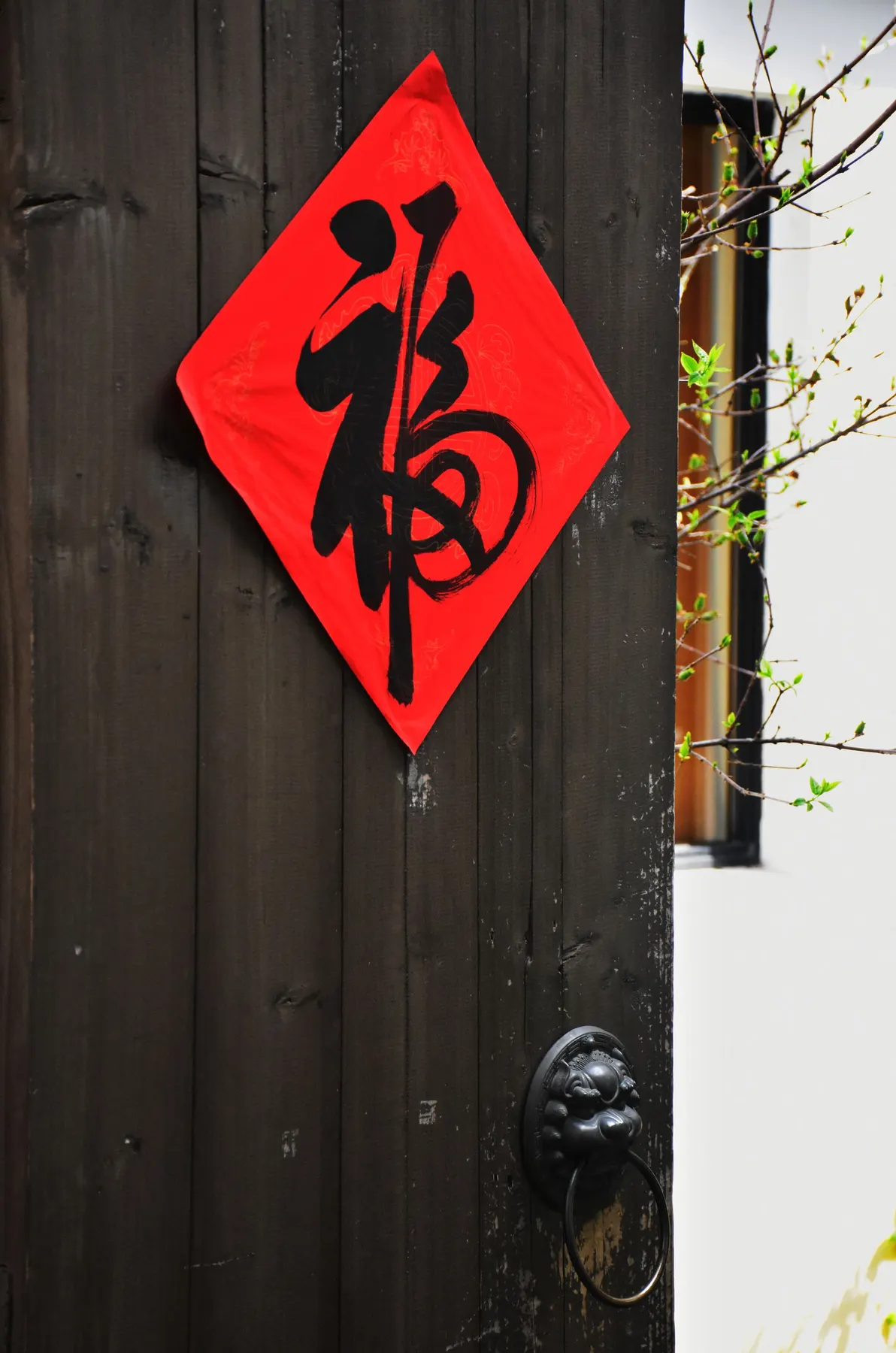 Red diamond paper with a black brushed fu character on a dark wooden door above a ring knocker