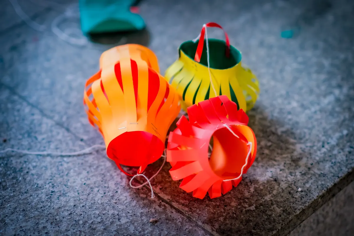 Three small cut-paper lanterns in red, orange, yellow and green resting on gray stone