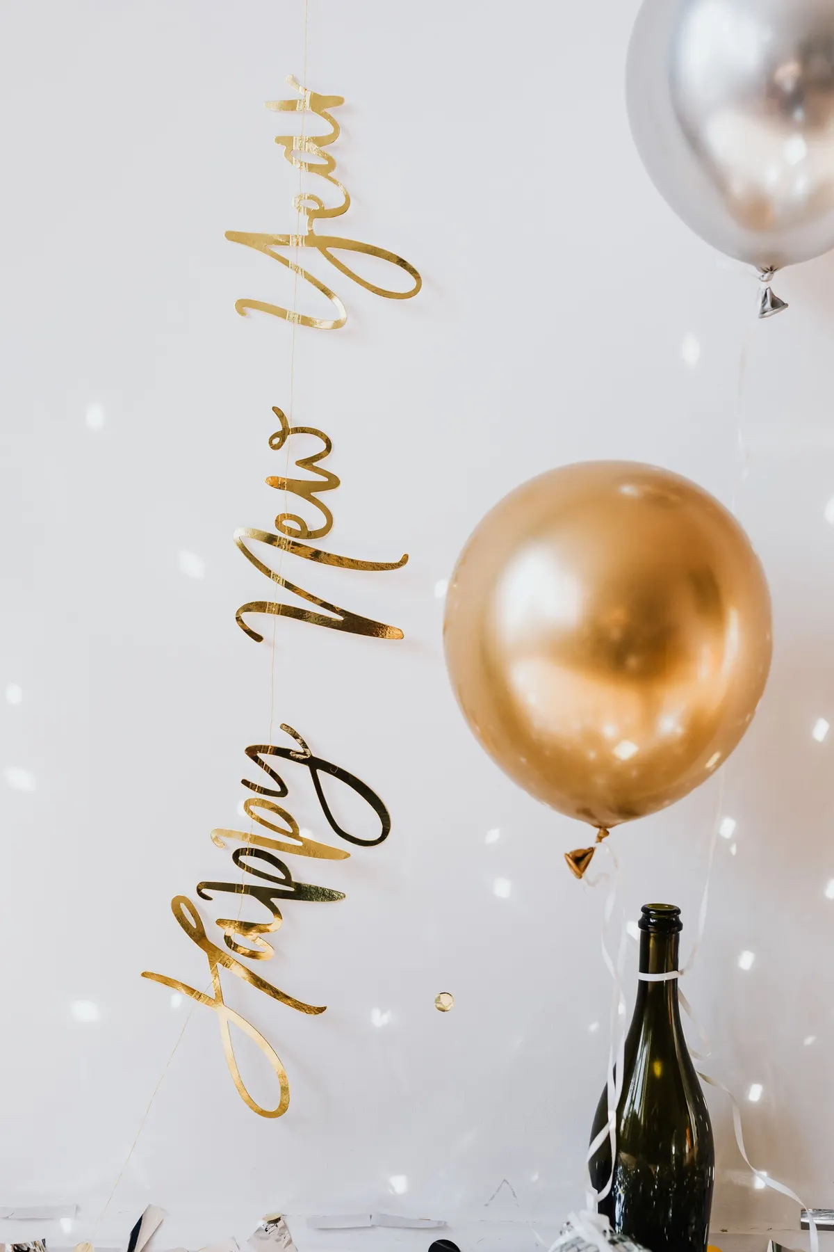 Gold script Happy New Year banner over a gold balloon, a silver balloon and a dark green bottle
