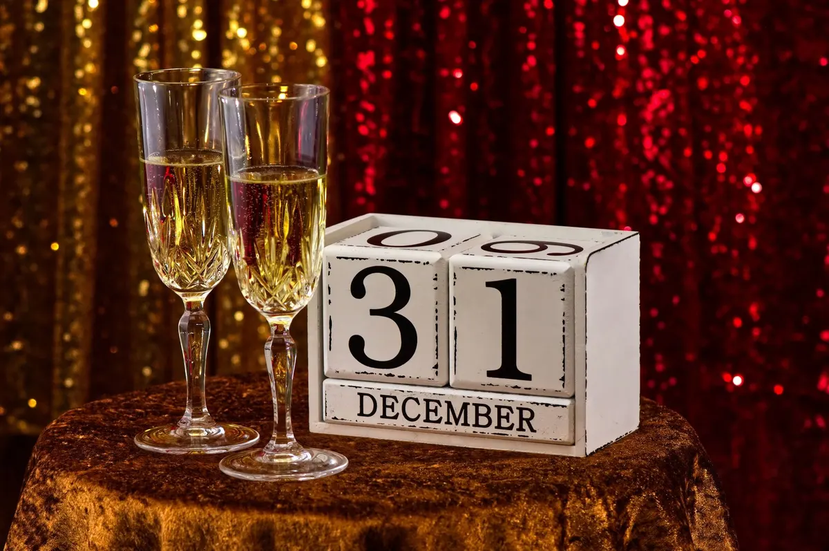 Two flutes of sparkling wine beside a white December 31 block calendar on a gold tablecloth
