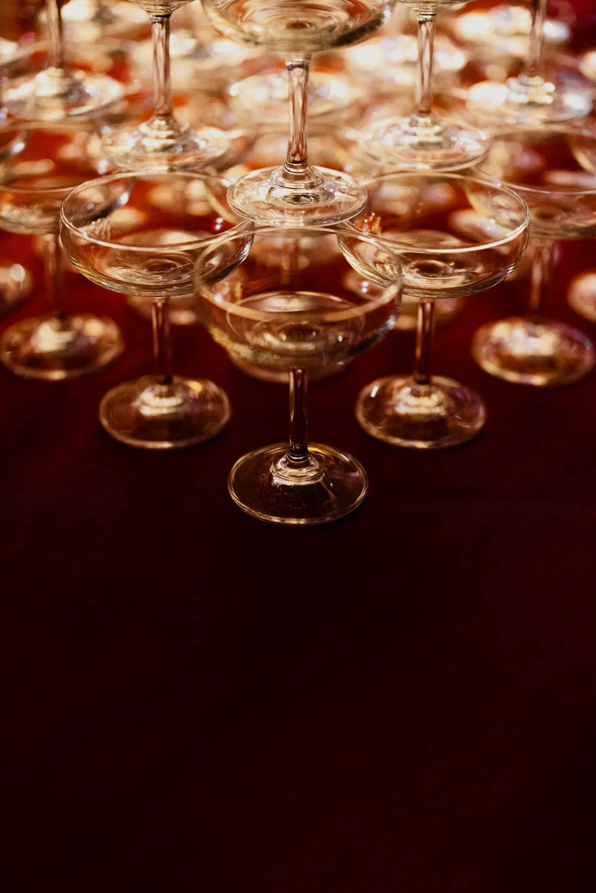 Stacked tower of clear coupe glasses on dark red fabric with soft gold reflections