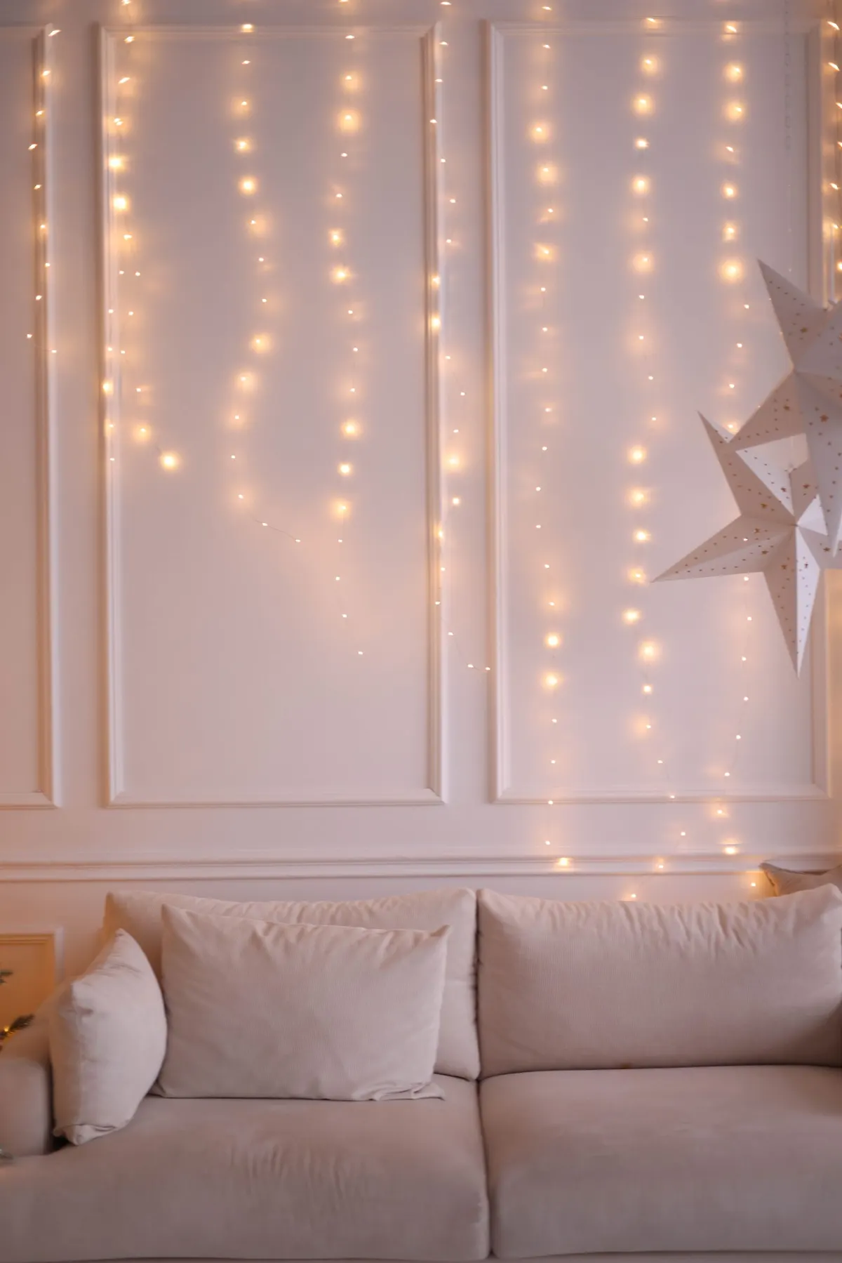 Cream sofa with soft pillows under warm white string lights and two white perforated paper stars