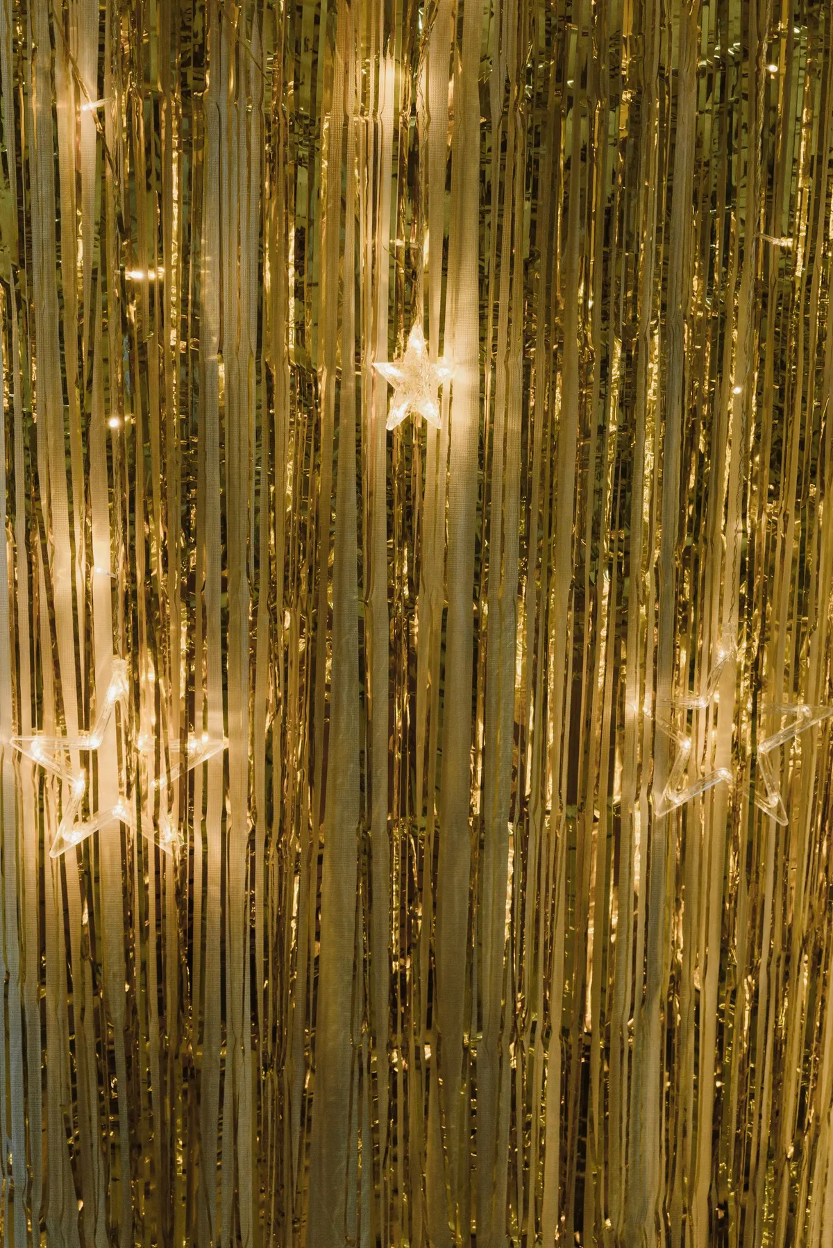 Gold fringe curtain with three glowing clear star lights and warm white string lights