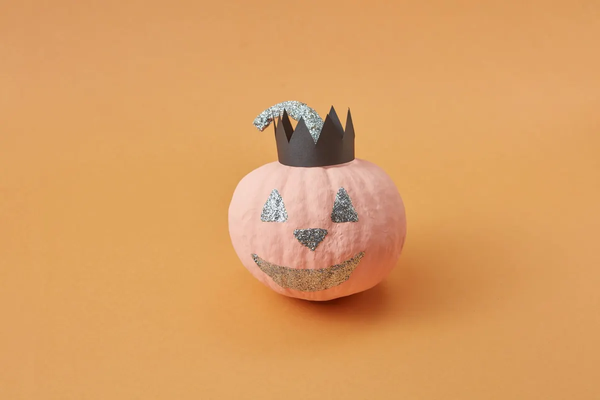 Small pale pink pumpkin with a silver glitter jack-o'-lantern face and glitter stem wearing a black paper crown