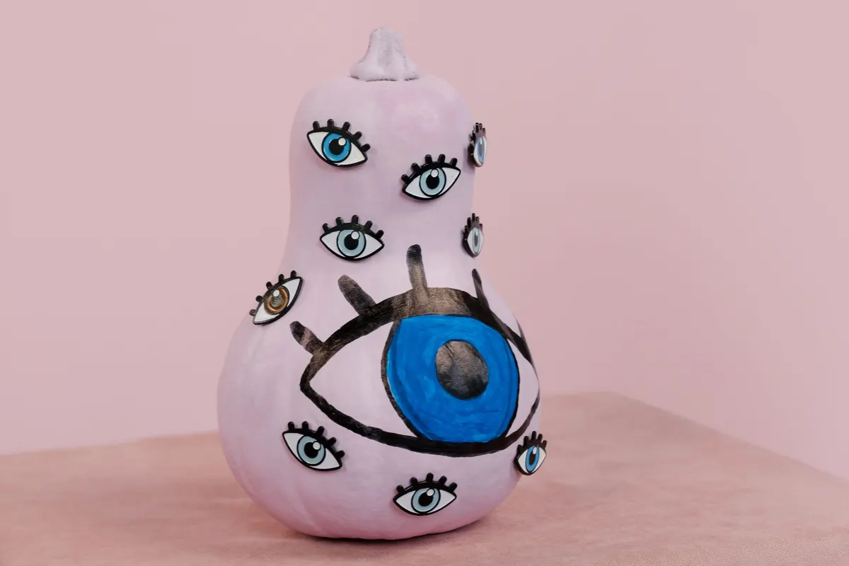 Lilac-painted butternut squash covered in small lashed eyes with one large blue eye on its lower bulb