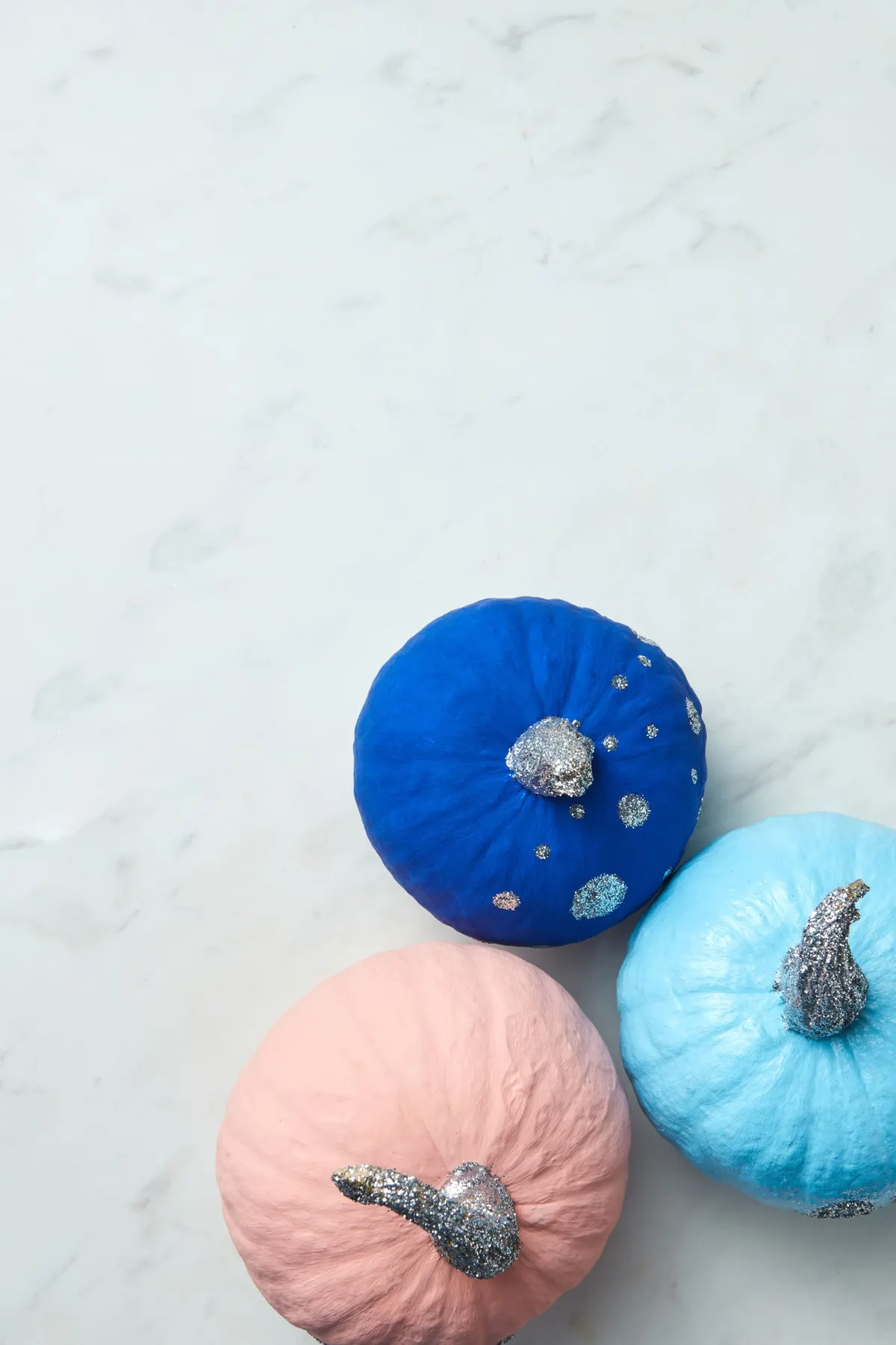 Three mini pumpkins painted royal blue with silver glitter dots, pale pink and sky blue, with glitter stems