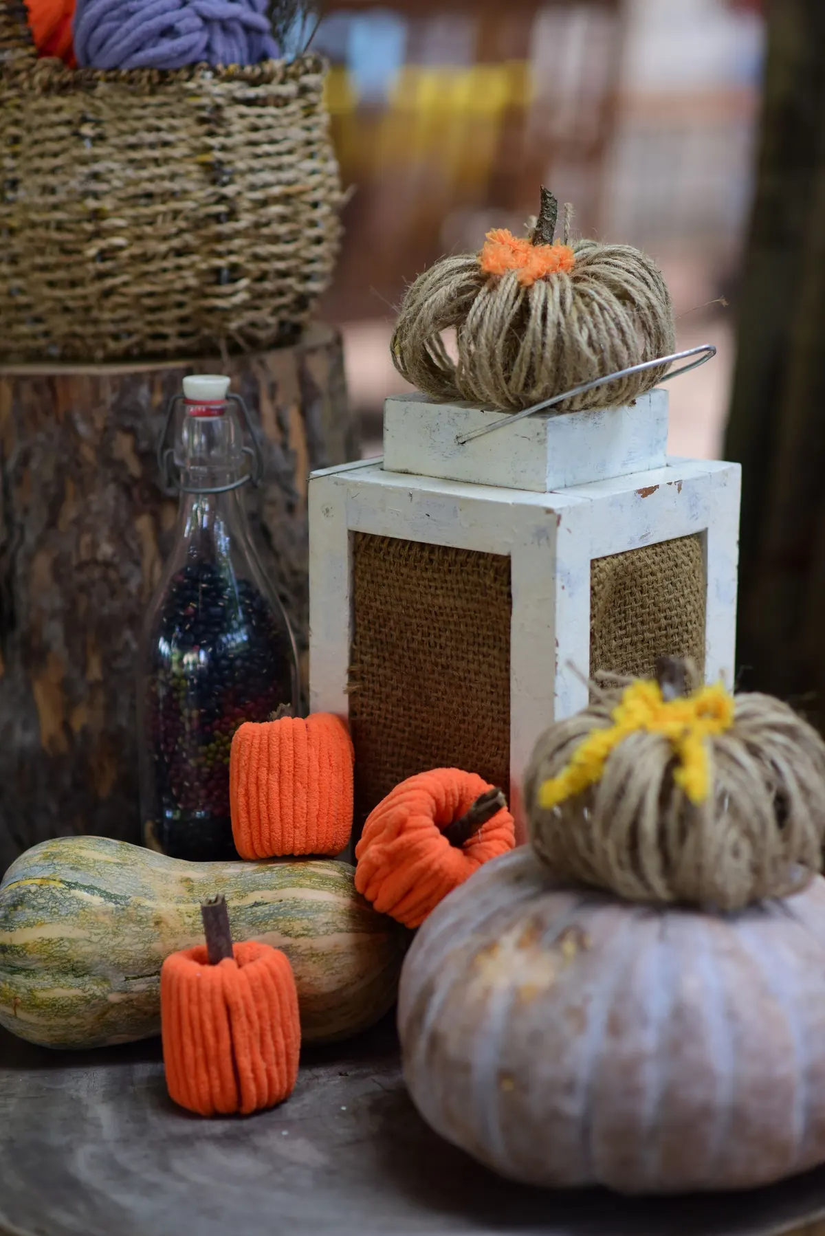 Two twine-wrapped pumpkins with yarn tufts, one on a white lantern, one on a lilac pumpkin, with knit minis