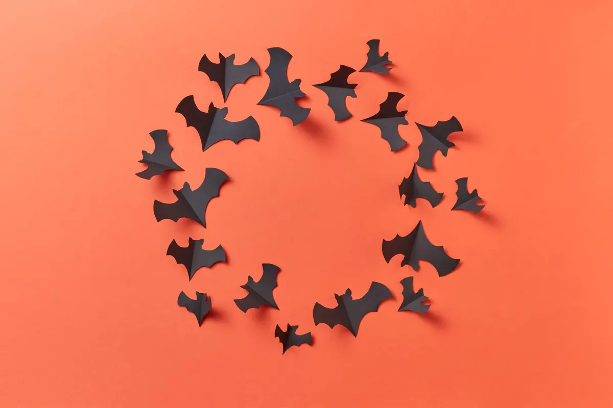 About twenty black paper bats with folded-up wings arranged in a loose ring on a coral orange background