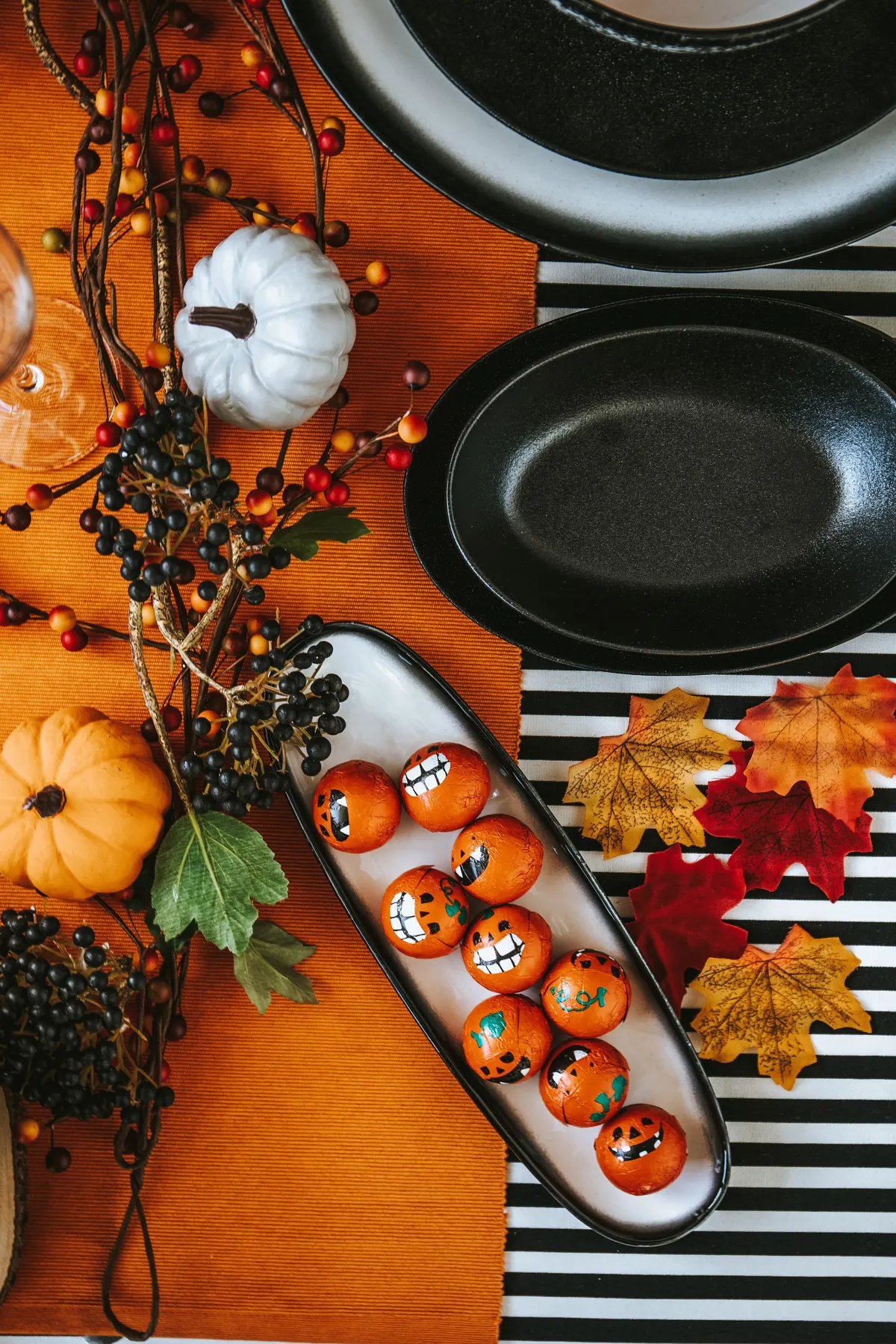 Overhead table with a striped cloth, a white platter of about nine orange round treats with jack-o'-lantern faces