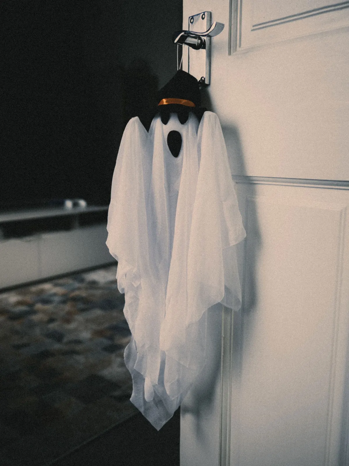 White sheer ghost with a black felt mouth and a small black witch hat, hanging from a silver door hook