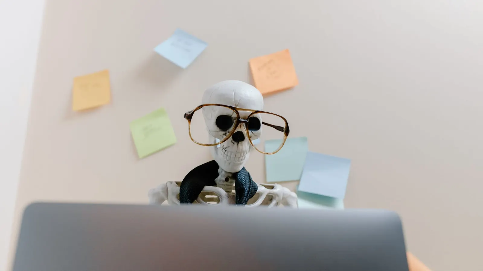 Plastic skeleton in round tortoiseshell glasses and a dark tie sits behind a gray laptop
