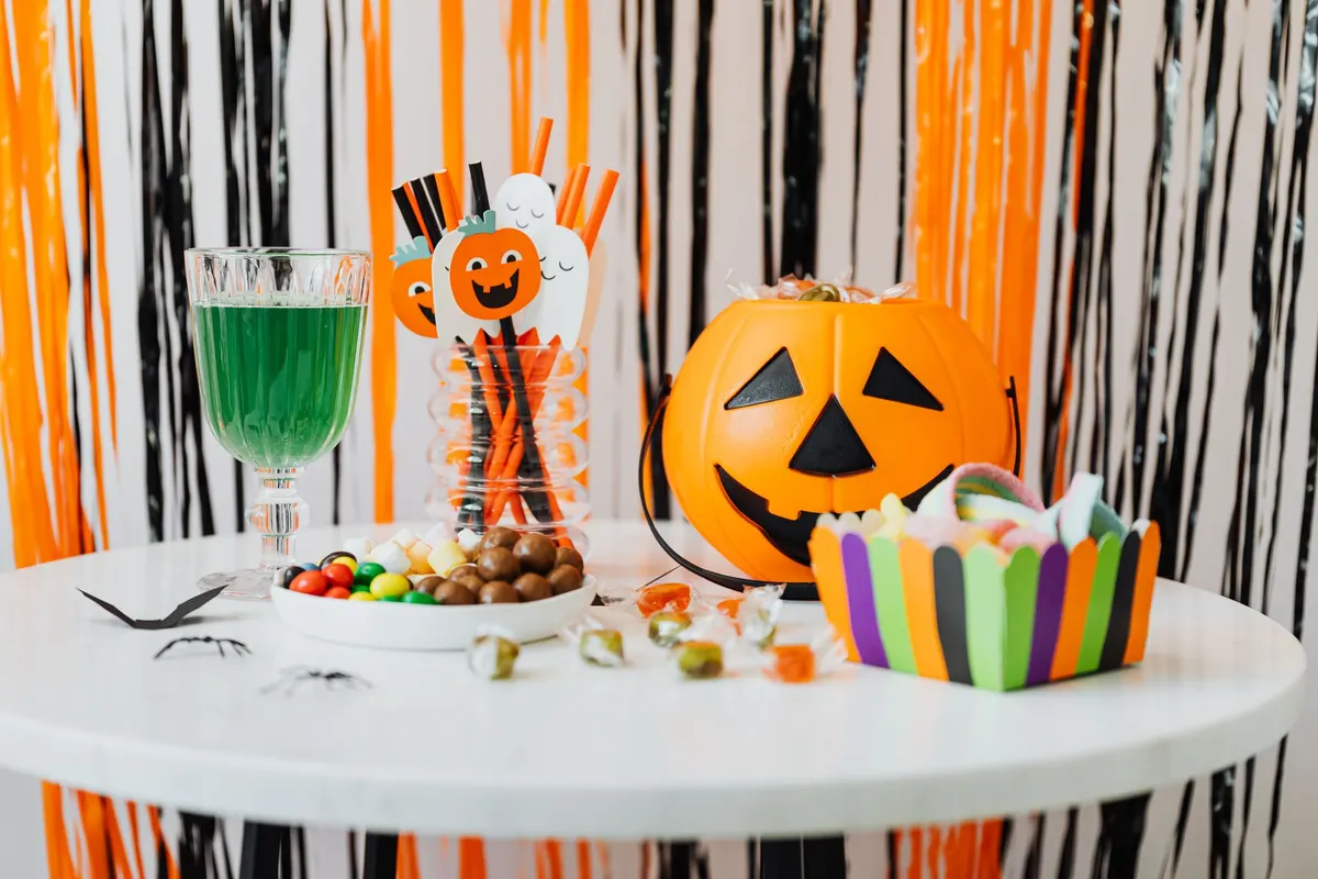 Round white table in front of an orange, black and white foil fringe curtain, with a jack-o'-lantern bucket