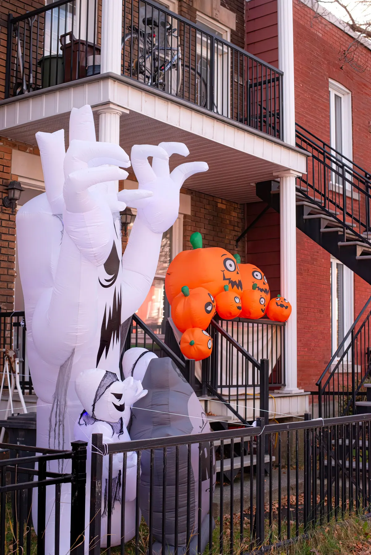 Tall white inflatable haunted tree, a small ghost, orange pumpkins and a gravestone in a small fenced front yard