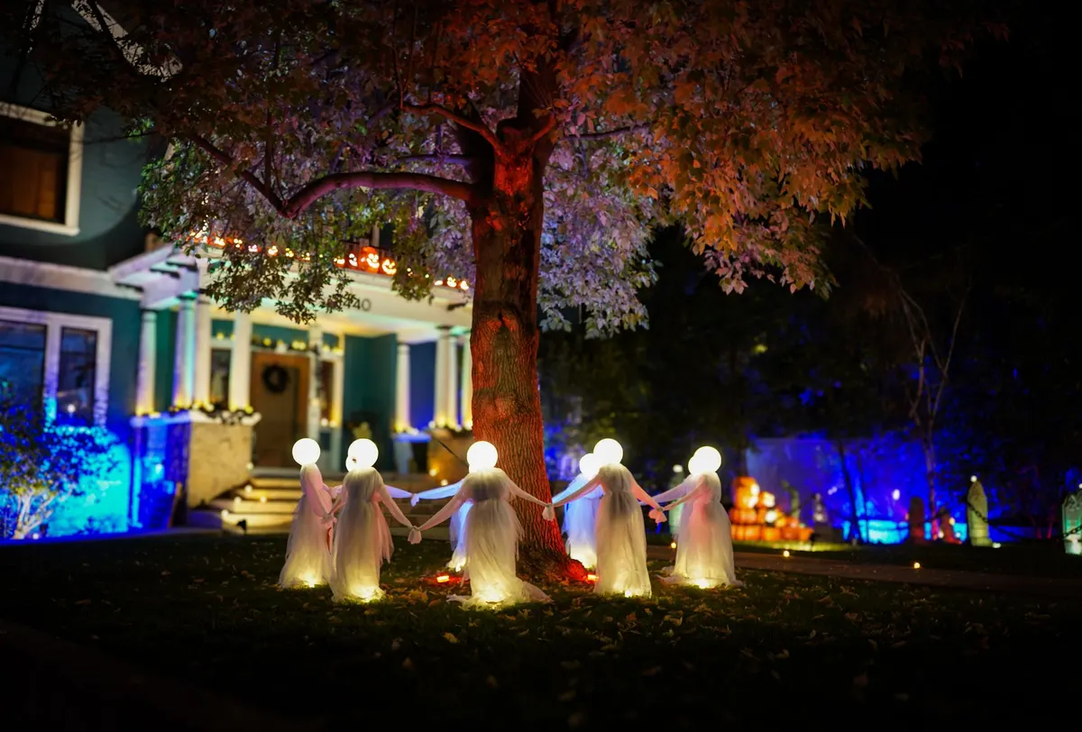 Glowing white ghosts with round lit heads holding hands in a ring around a large tree at night