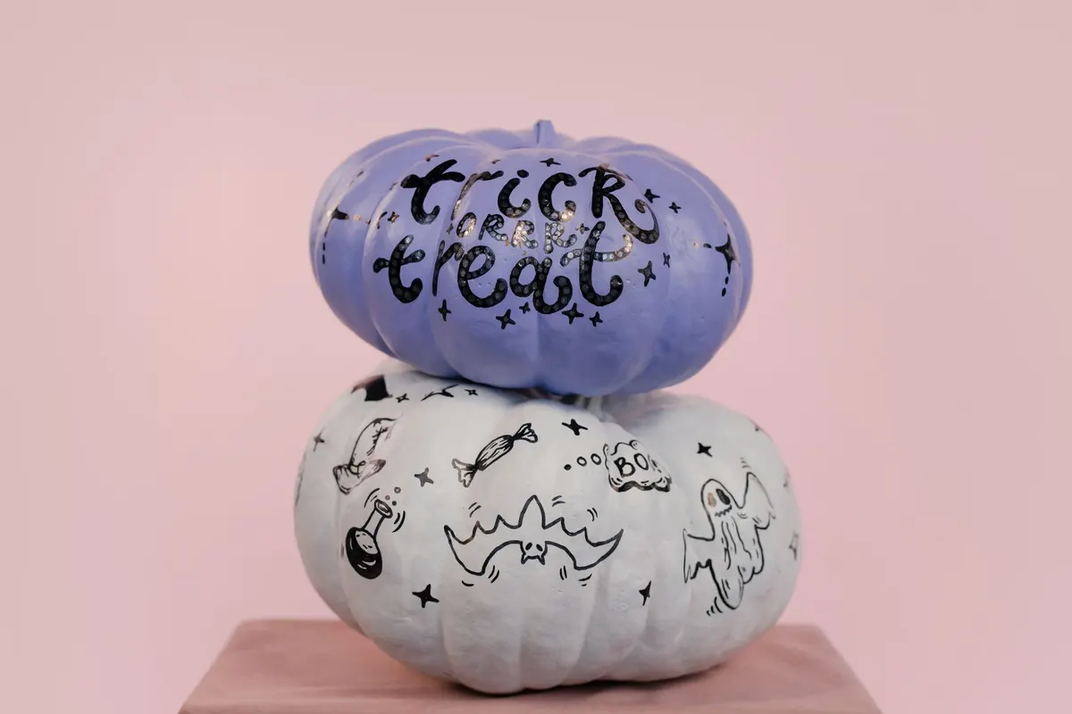 White pumpkin covered in black marker doodles of a witch hat, potion flask, candy, bat and ghost