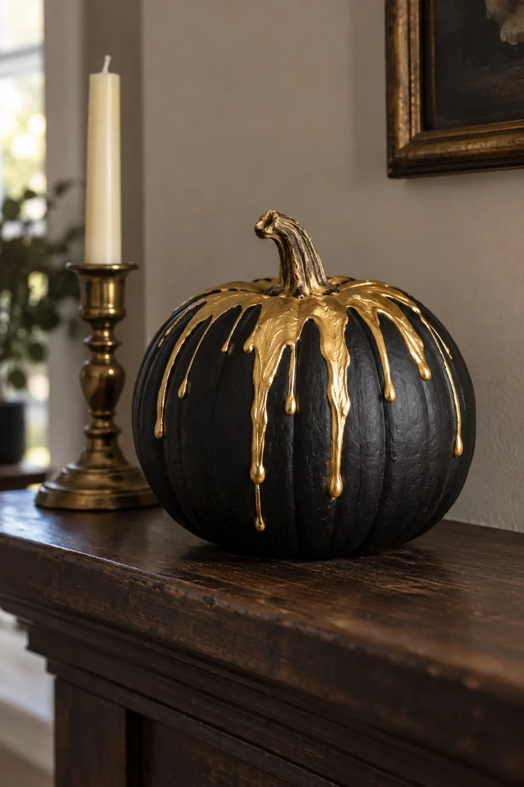 Matte black pumpkin with metallic gold splashed across the top and dripping down the sides, beside an ivory taper candle