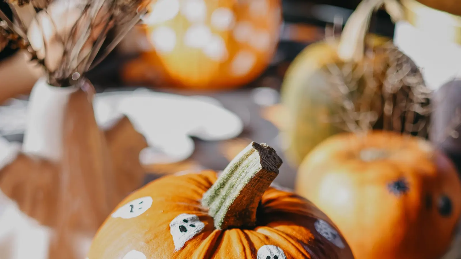 Large orange pumpkin covered in about fifteen small white painted ghosts with black dot eyes and open mouths