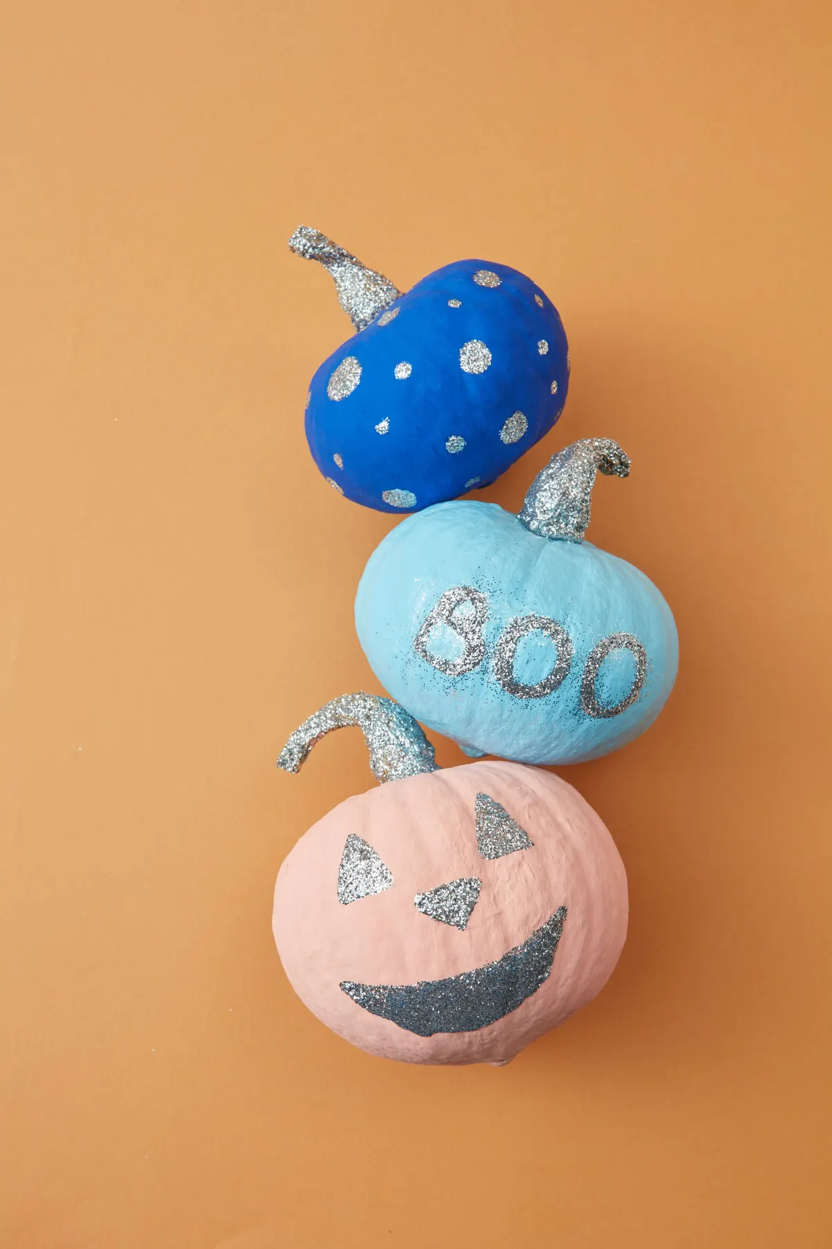 Three small pumpkins in a row: royal blue with silver dots, aqua with silver BOO letters and peach pink