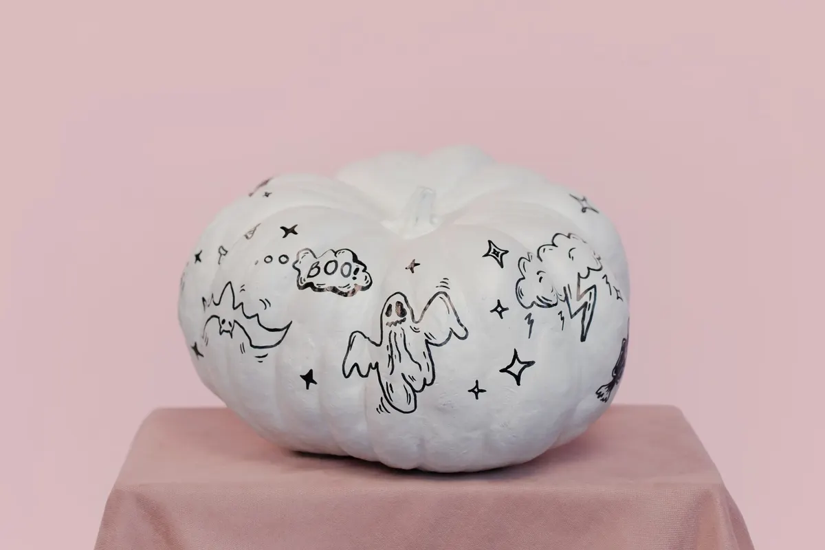 White pumpkin painted with a big black-outlined sheet ghost, a small flying ghost, a BOO speech bubble